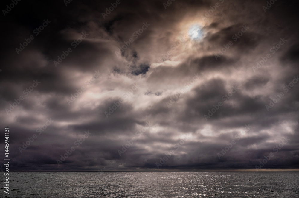 Sun between dark storm clouds over ocean. Dramatic seascape. Clouds and rain flurry over sea.