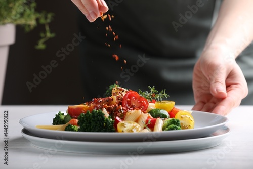 Fototapeta Naklejka Na Ścianę i Meble -  Woman sprinkling spices onto pasta with vegetables at white table indoors, closeup
