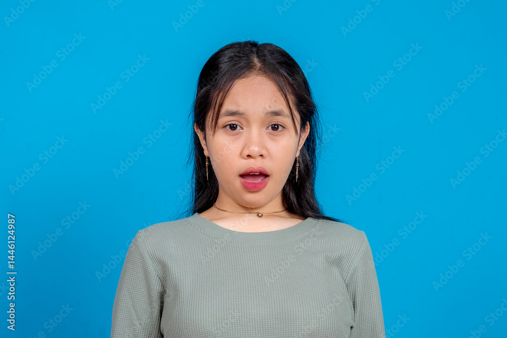 Portrait of a young Asian woman expressing shock and surprise with wide eyes and open mouth. Isolated on blue background. Concept of disbelief, astonishment, and reaction. Portrait of a young Asian woman expressing shock and surprise with wide eyes and open mouth. Isolated on blue background. Concept of disbelief, astonishment, and reaction.
