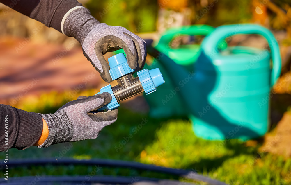 Closeup of hands in the gloves. Process of installing fittings pipes and connectors for the garden and lawn irrigation system installation. Green grass, shallow depth of field.