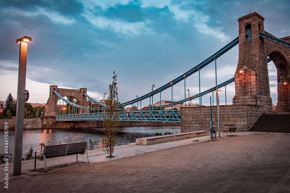 Fototapeta premium A beautiful urban bridge over the river and a quiet, deserted waterfront with soft evening lighting.