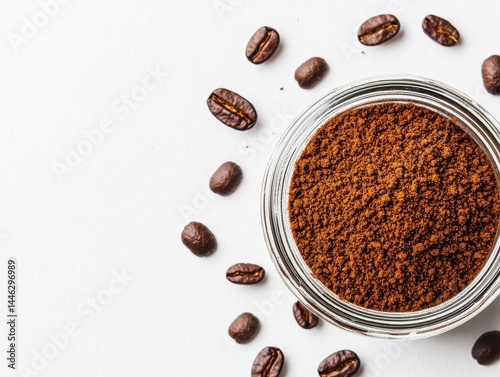 A glass jar of ground coffee surrounded by scattered coffee beans on a white background.