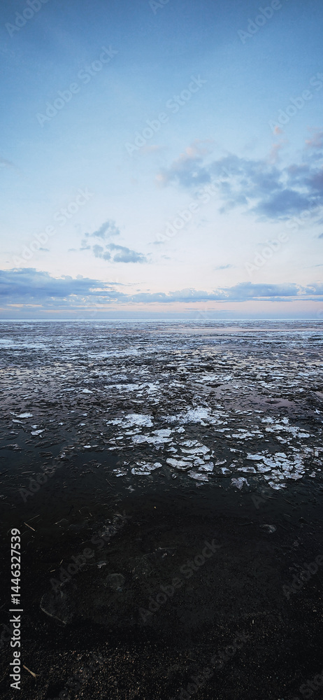 Spring landscape. Panoramic view of beautiful dawn on bay. Cumulus clouds over water in bright light. Ice, snow and rocks on coastline. Rising rays of sun are reflected in sea. Vertical photo Spring landscape. Panoramic view of beautiful dawn on bay. Cumulus clouds over water in bright light. Ice, snow and rocks on coastline. Rising rays of sun are reflected in sea. Vertical photo