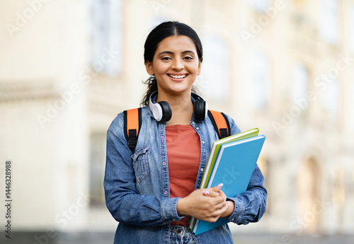 Positive young indian woman student wearing casual outfit with backpack and notepads exercise books posing outdoor at university campus, smiling at camera, copy space. Students lifestyle