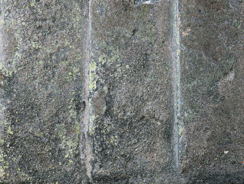 Top view close-up of gray weathered textured stone surface with chisel marks, cracks, holes, moss, mossy green lichen. Texture background of aged rough grey imprinted concrete floor slabs blocks. 