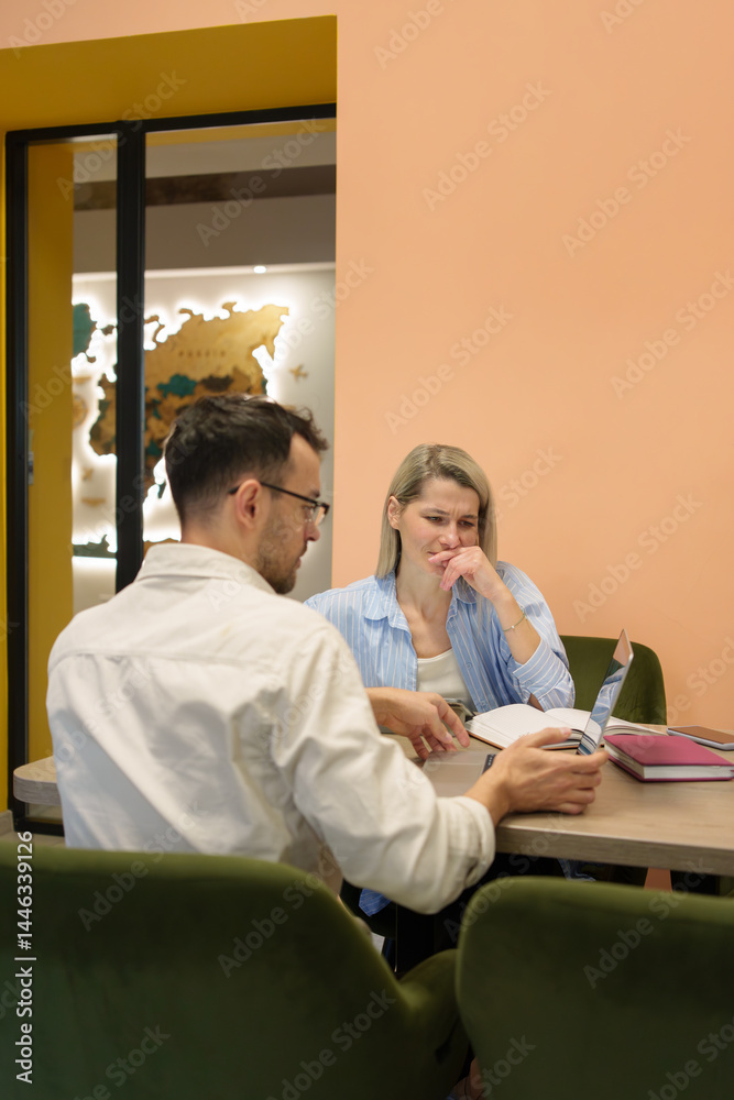 Obraz premium Two professionals collaborating in an office environment, reviewing documents and discussing ideas.