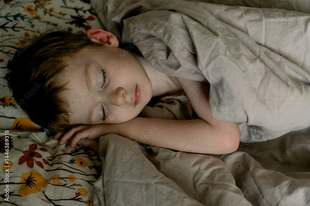 Obraz premium Little boy sleeping on a floral pillow and covered with a beige blanket. Cozy home concept.
