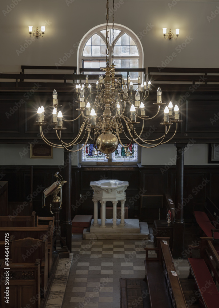 Stunning view of Chandelier hanging from the ceiling over white octagonal baptismal font inside of The Church of King Charles the Martyr, is a Church of England parish church in Royal Tunbridge Wells.