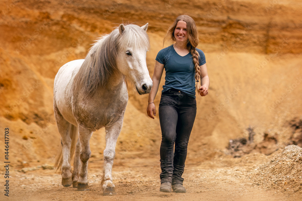 A young woman and her white icelandic horse gelding interacting in a sand pit; horsemanship concept