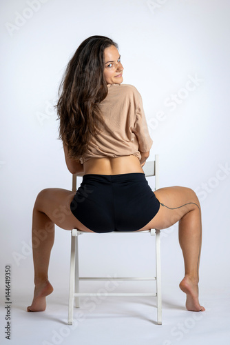 Young women posing with short shirt on a chair.