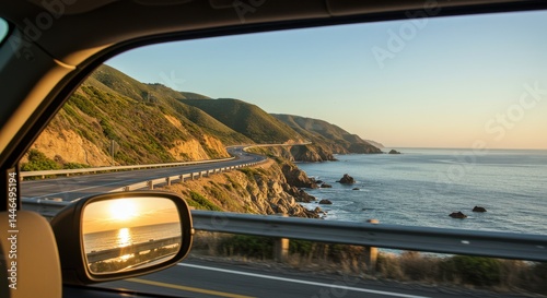 Coastal road at sunset viewed from the driver's seat of a vehicle with side mirror reflecting the ocean