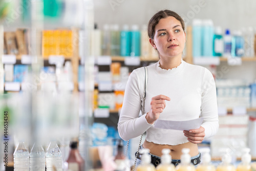 Girl with medical prescription in hand looking for medicine in modern pharmacy photo