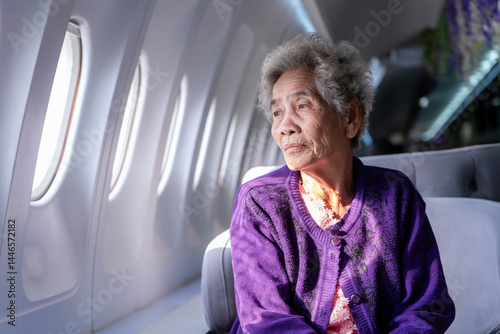 Senior Asian gray haired woman looking out the airplane window. Portrait of an elderly woman sitting in a window seat of an airplane