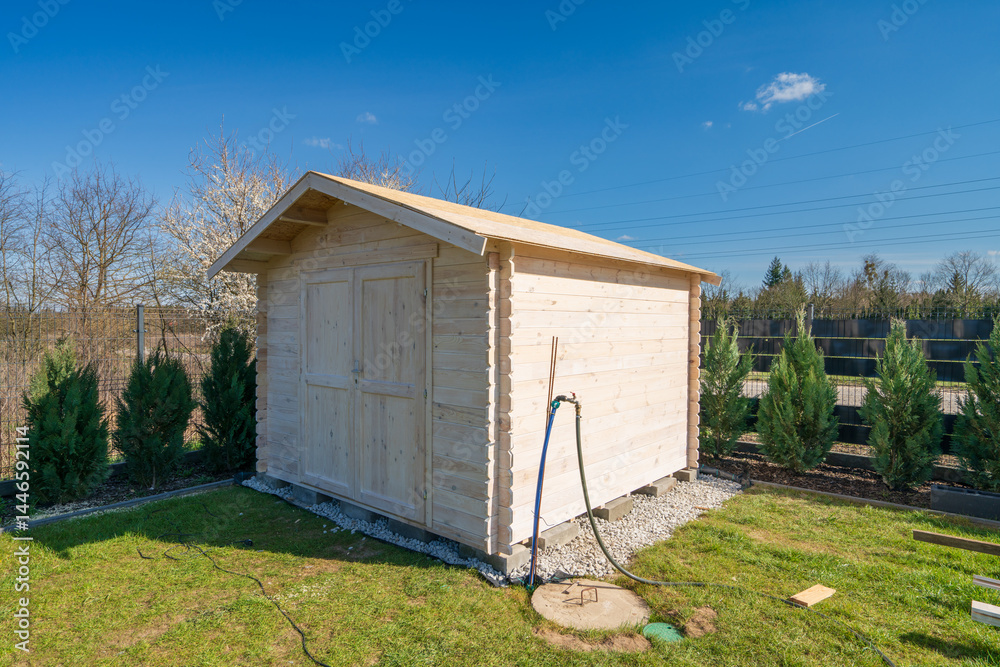 Wooden unpainted shed in the garden under clear blue sky