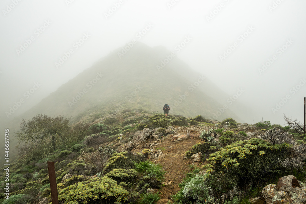 Mountains Loom Behind Woman Hiking Uphill in Fog