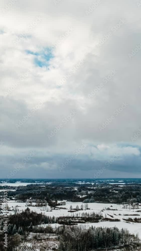 Vertical aerial winter hyperlapse in countryside with snow covered forest and moving clouds. Drone timelapse in winter.