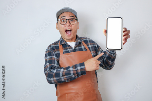 Surprised young Asian man barista barman employee wearing brown apron work in coffee shop using mobile phone isolated on white background. Small business startup concept