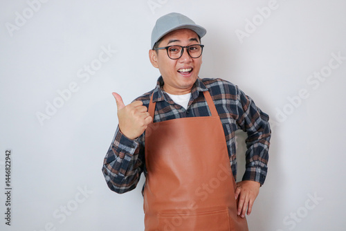 Asian barista man wearing apron and cap smiling and showing thumb up isolated over white background