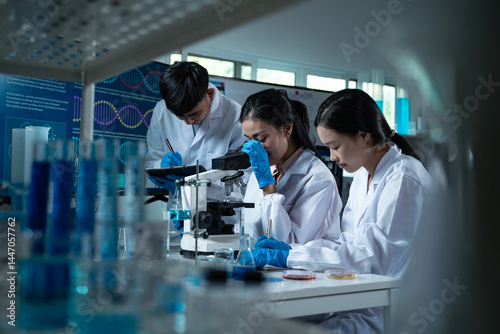 Three young scientists in lab coats working together in a laboratory examining a petri dish for microbiology biology and medical research with focus on education and innovation