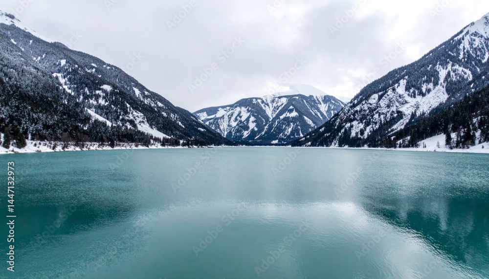 Obraz premium tranquil teal lake surrounded by majestic snow capped mountains creates serene winter landscape. calm water reflects beauty of nature, inviting peace and contemplation