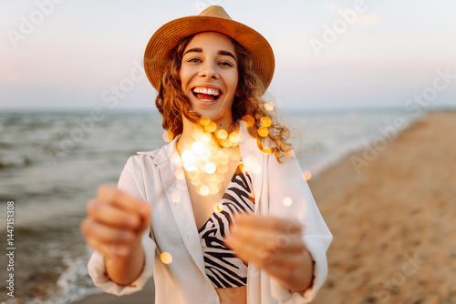 Wallpaper Mural Happy woman in hat enjoying sunset on beach with sparklers in hands. Young woman having fun with sparklers outdoors. Holiday and recreation concept. Torontodigital.ca
