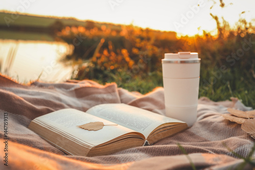 Slika na platnu Open Bible and takeaway cup on cozy plaid blanket at riverside during golden sunset