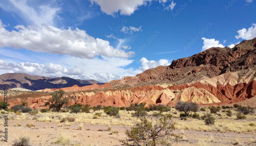 Background shows vibrant red rock formations and sparse desert vegetation under a bright blue sky with scattered fluffy clouds. Background shows vibrant red rock formations and sparse desert vegetation under a bright blue sky with scattered fluffy clouds.