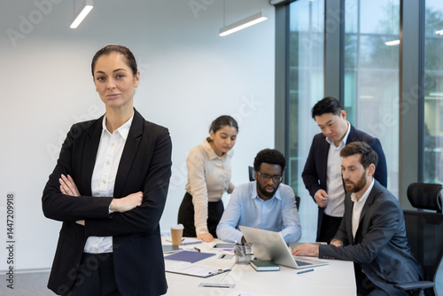 A confident businesswoman stands in front of a diverse team, illustrating corporate collaboration and leadership. They discuss business and work.