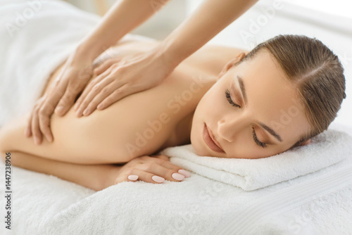 Indoor shot of relaxed woman enjoying spa treatment in salon, getting massage for back, has body care treatment, lying on white towel. Setting evoking sense of serenity and wellbeing