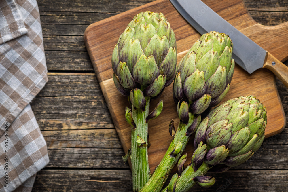 Fototapeta premium Ripe artichokes plant on cutting board. Top view.