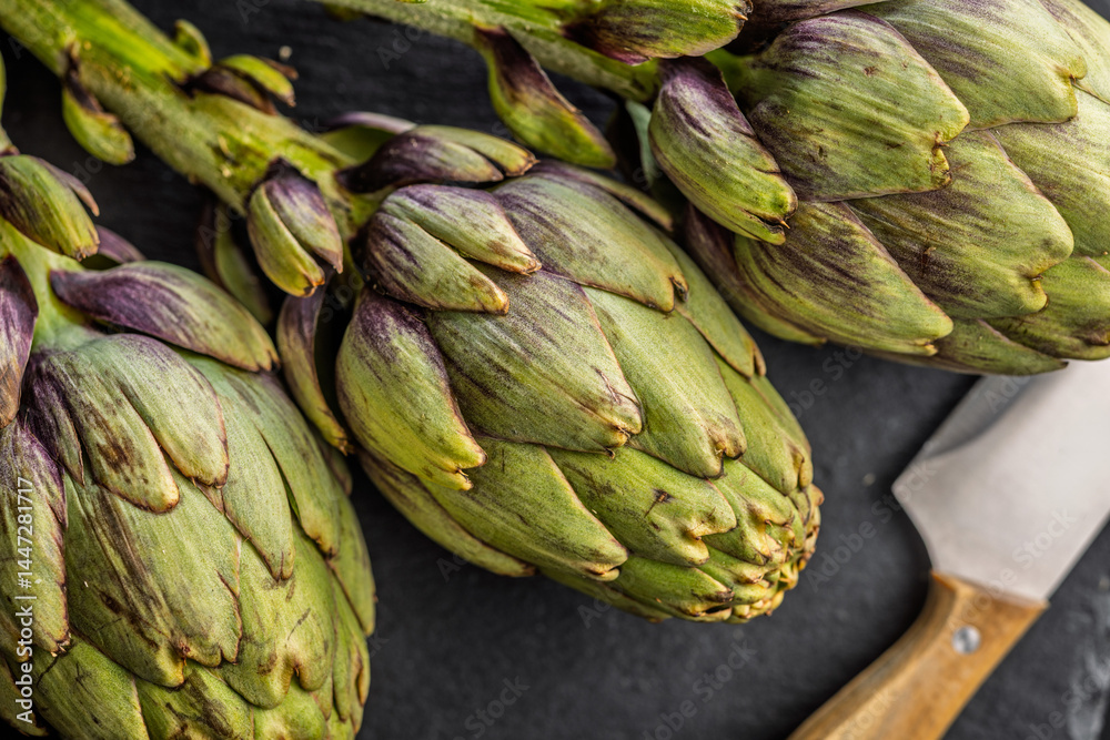 Obraz premium Ripe artichokes plant on cutting board. Top view.
