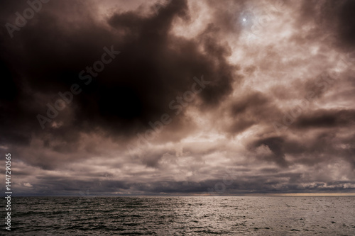 Sun between dark storm clouds over ocean. Dramatic seascape. Clouds and rain flurry over sea.