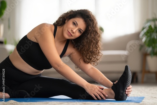 Young Hispanic woman with long curly hair stretching on a blue yoga mat in a bright living room,