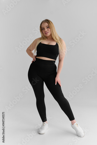 Cute girl with blond hair in tracksuit on white background. Fat middle-aged lady posing in tight clothes in studio. Body positivity concept