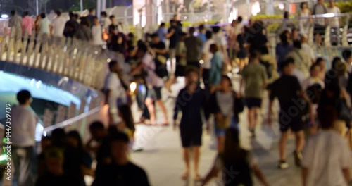 Blurred view of busy pedestrian bridge with tourist walking forth and back. People exploring Singapore downtown at late evening in summer day. Typical crowded area of touristic place of the city