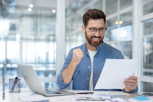 Cuadro en lienzo A happy man is celebrating a win at the office, excited with his paperwork, and clenching his fist