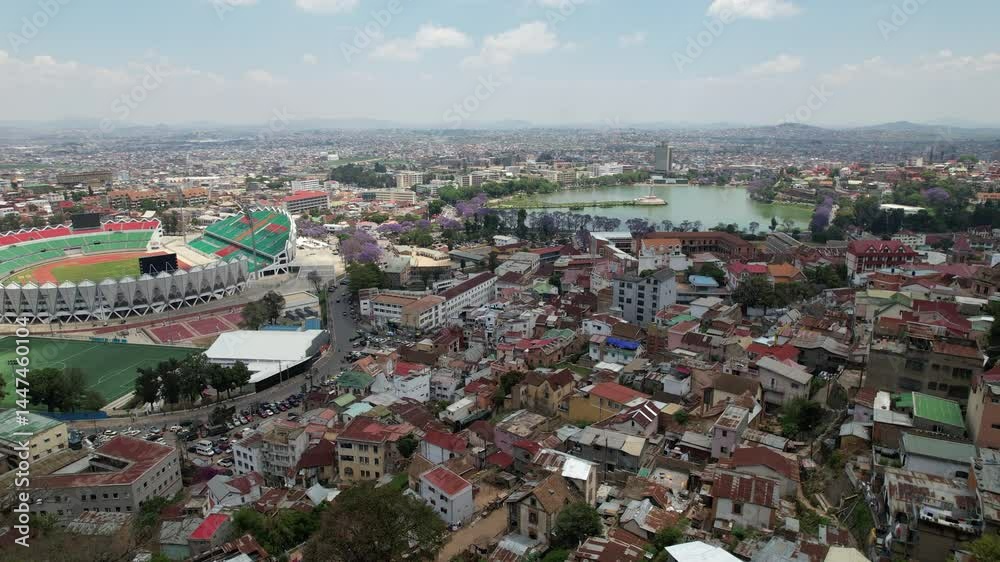 Forward drone approach highlighting Lake Anosy and Barea Stadium in Antananarivo, Madagascar, surrounded by jacaranda trees and cityscape. Exported in 4K ProRes.