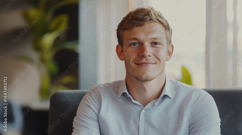 Naklejka premium Happy young man smiling, seated in a comfortable chair indoors.