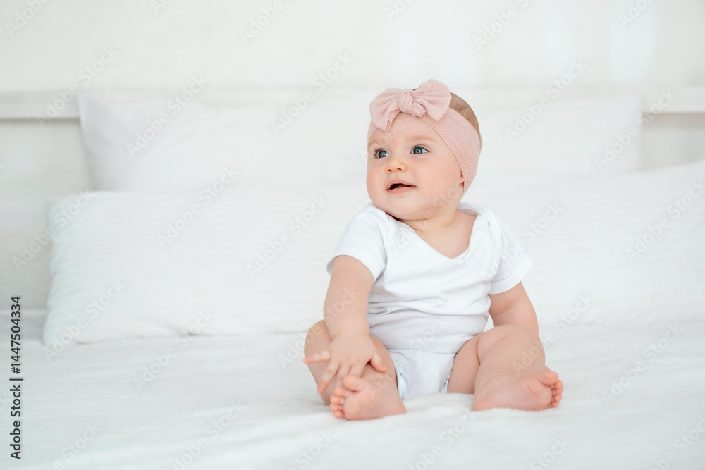 A baby girl is smiling at home on a white bed with a bow on her head, a happy healthy child of six months is laughing A baby girl is smiling at home on a white bed with a bow on her head, a happy healthy child of six months is laughing