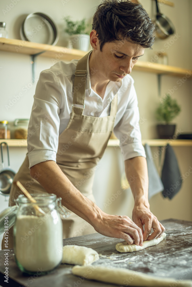Fototapeta premium A baker in an apron kneads the dough with his hands and sprinkles it with flour to bake delicious homemade bread.