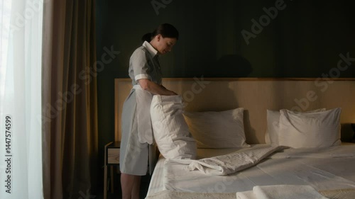 Wallpaper Mural Hotel room attendant in uniform putting pillowcase and fluffing pillow while making guest bed Torontodigital.ca