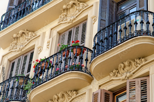 Picturesque balconies with iron railings and blooming flowers decorate a historic European apartment facade. Evokes a romantic urban atmosphere and architectural charm.