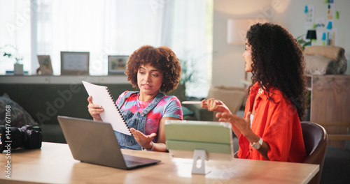 Women, documents or discussion with laptop for small business, budget or expenses at home. Female people, freelancers or remote workers with paperwork, technology or cost for online startup at house