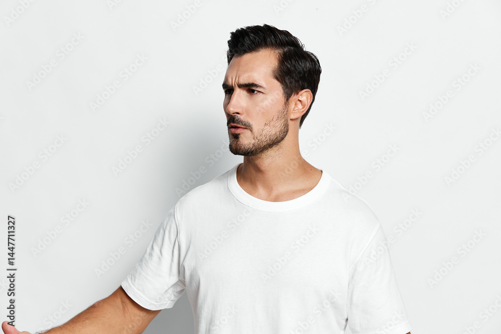 Stylish man with a serious expression wearing a plain white t-shirt, posing confidently with his hand raised, isolated on a minimalist solid background. Fashion portrait concept. Stylish man with a serious expression wearing a plain white t-shirt, posing confidently with his hand raised, isolated on a minimalist solid background. Fashion portrait concept.