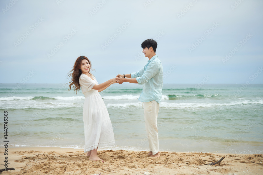 Young Asian Man and Woman Dancing Joyfully Together on Sandy Beach by the Ocean Young Asian Man and Woman Dancing Joyfully Together on Sandy Beach by the Ocean
