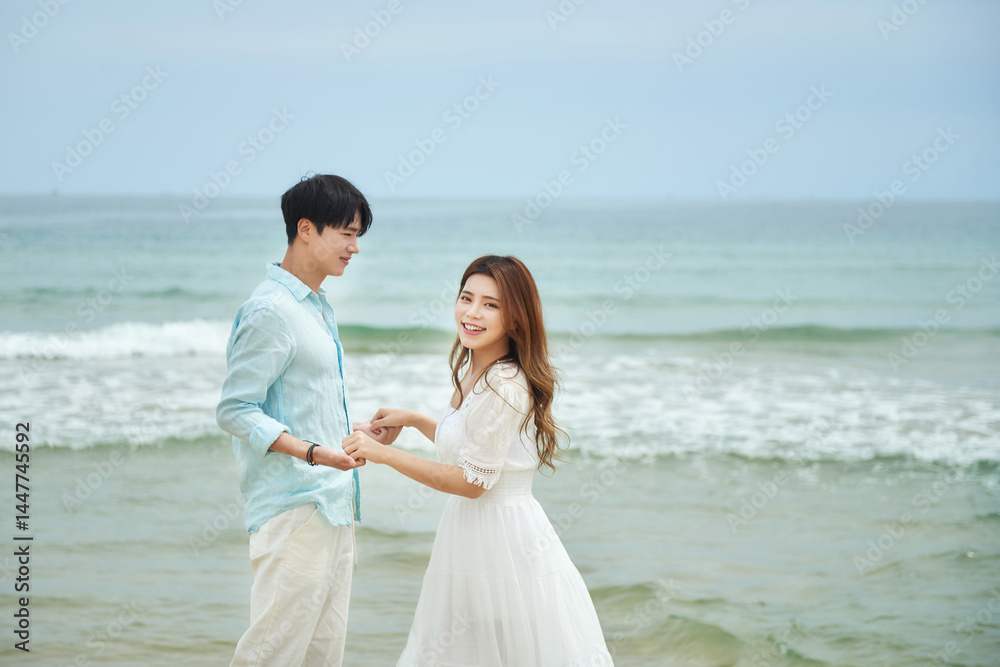 Young Asian Man and Woman Dancing Joyfully Together on Sandy Beach by the Ocean Young Asian Man and Woman Dancing Joyfully Together on Sandy Beach by the Ocean