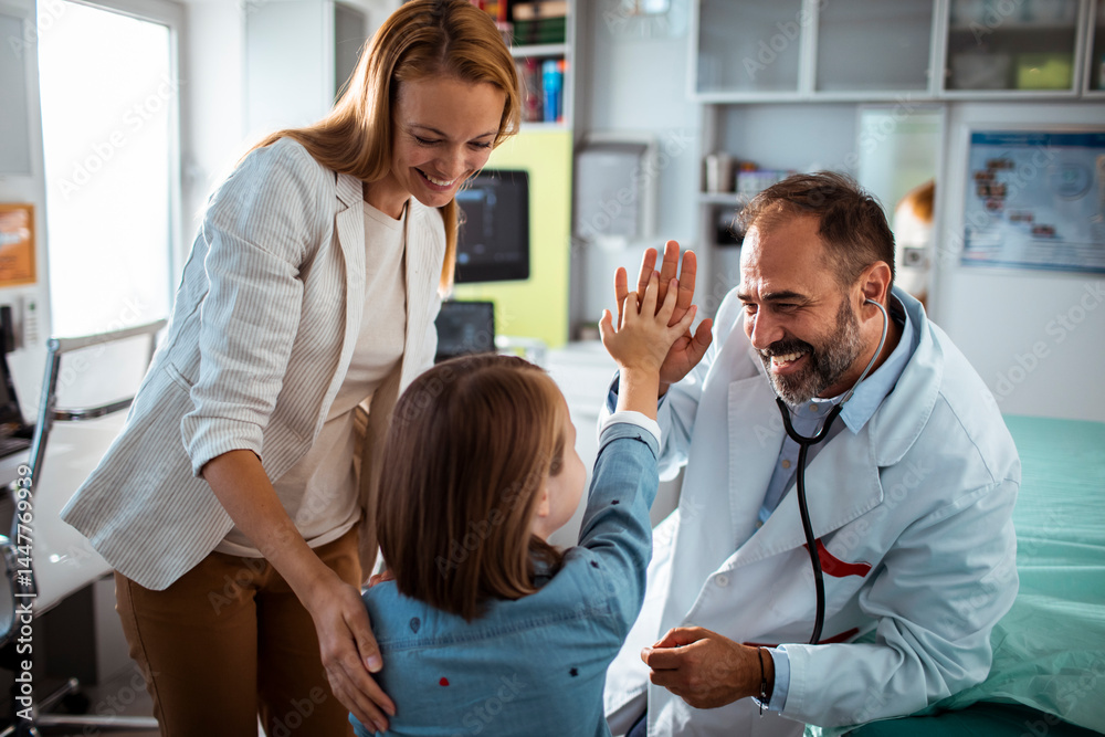 Smiling doctor using stethoscope to check young girl at medical clinic with mother nearby Smiling doctor using stethoscope to check young girl at medical clinic with mother nearby