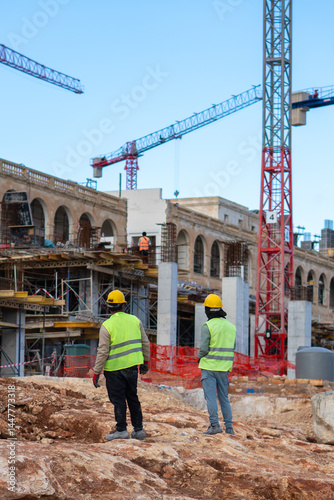 Two construction workers working at site of a large building project, Work overtime at construction site,Team of engineer discus at site