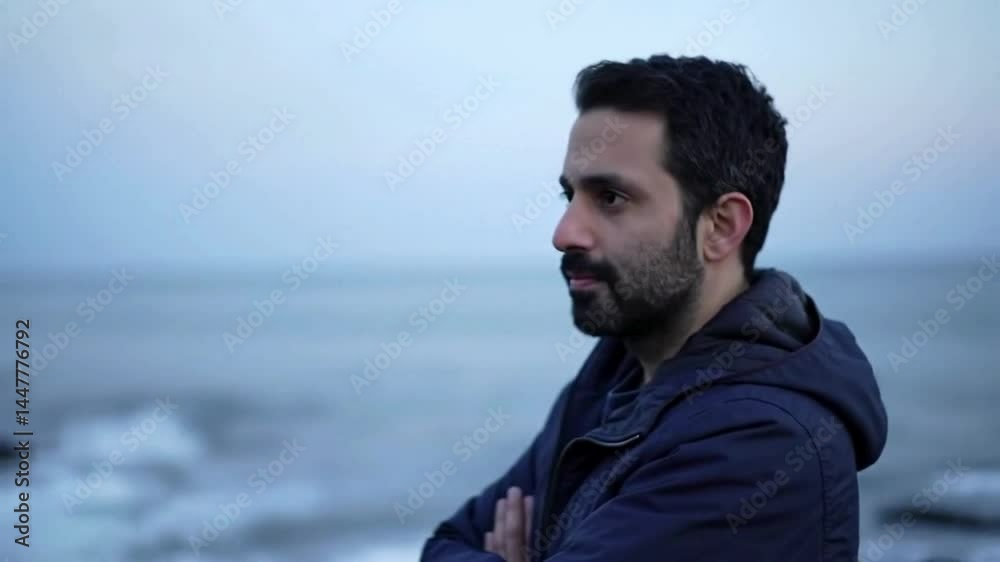 Man looking at sea on overcast day with waves and rocks in foreground Man looking at sea on overcast day with waves and rocks in foreground