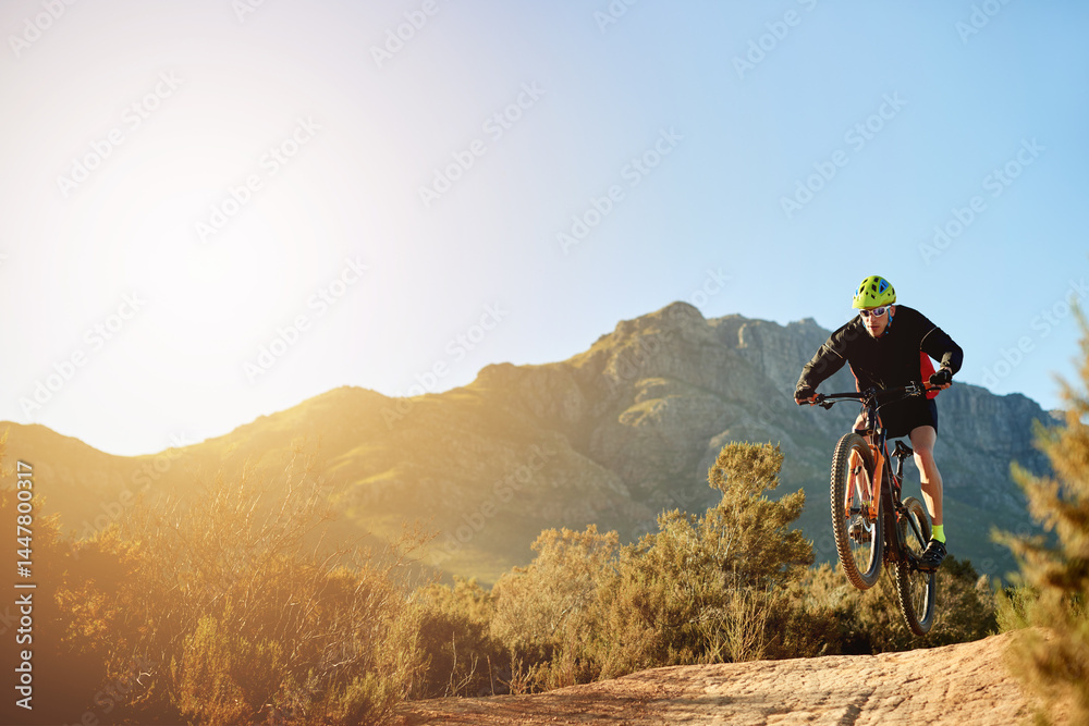 Naklejka premium Man, mountain bike and jump with sunset on dirt road for adrenaline rush, fitness or extreme sport in nature. Male person, cyclist or riding with bicycle for stunt or cardio on path, trail or space